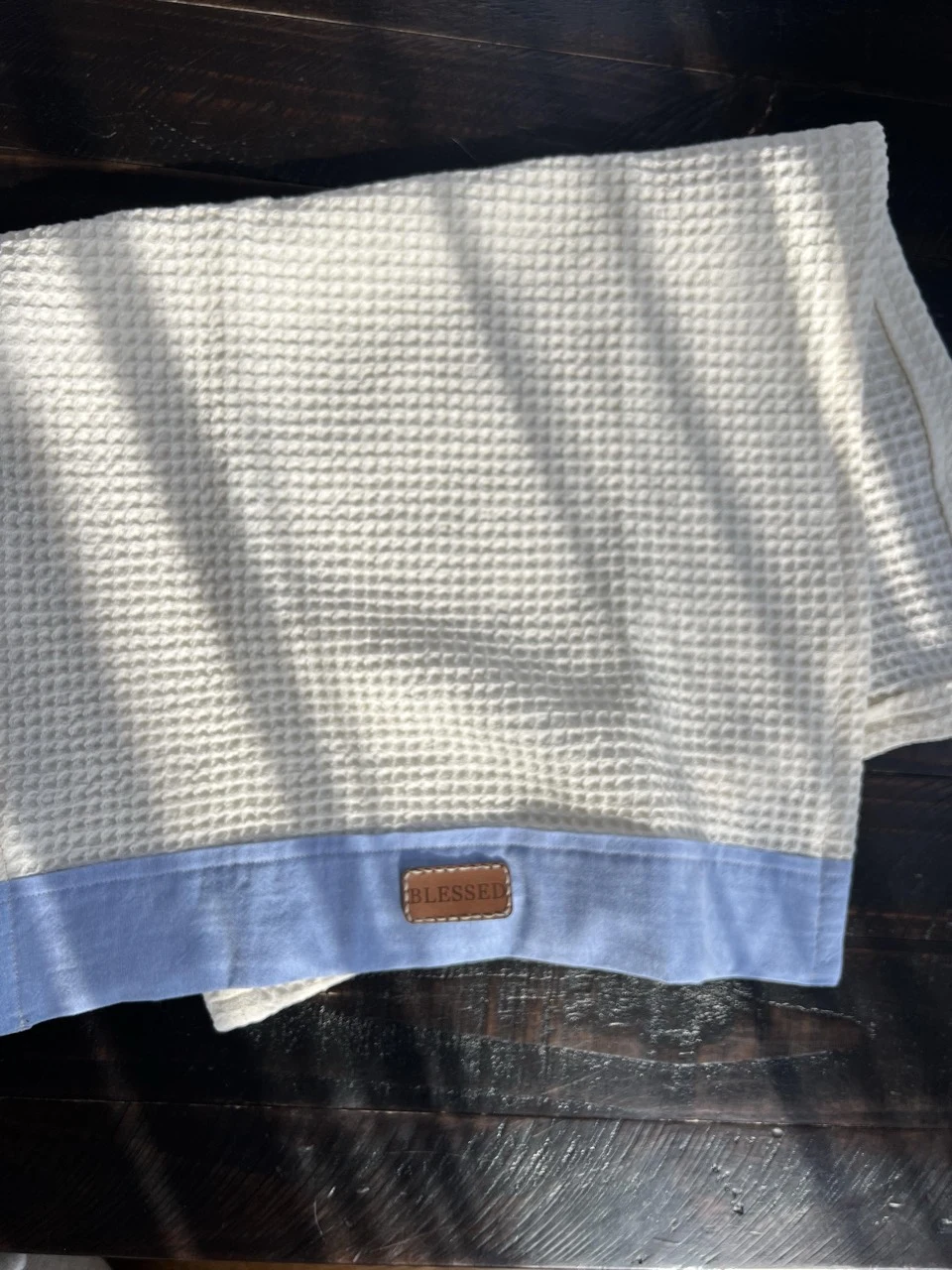 Cream waffle-textured towel with a blue border and Blessed message patch laid on dark wood