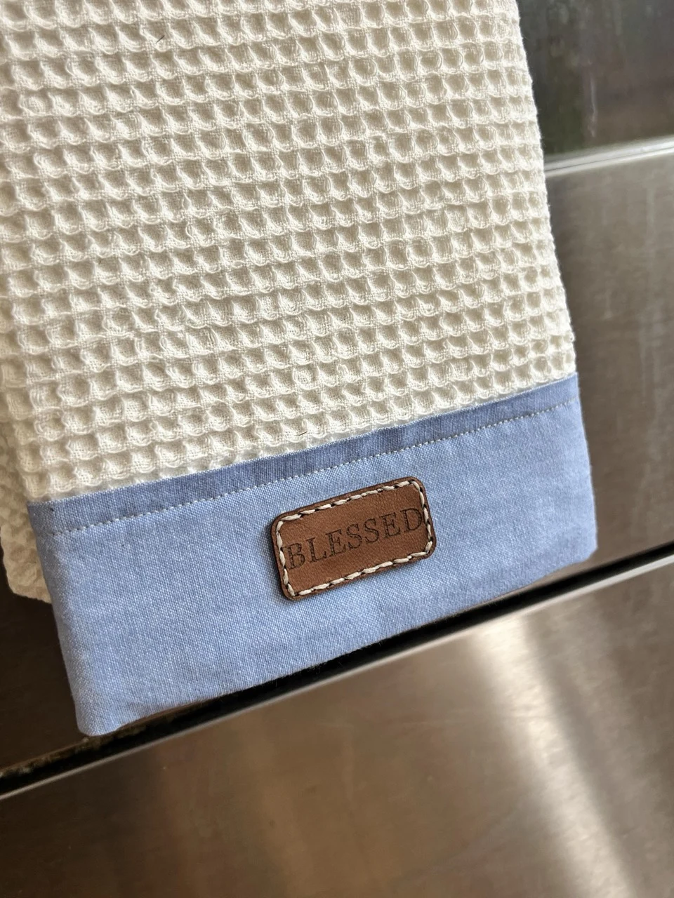 Blessed tea towel hanging against a stainless steel kitchen appliance